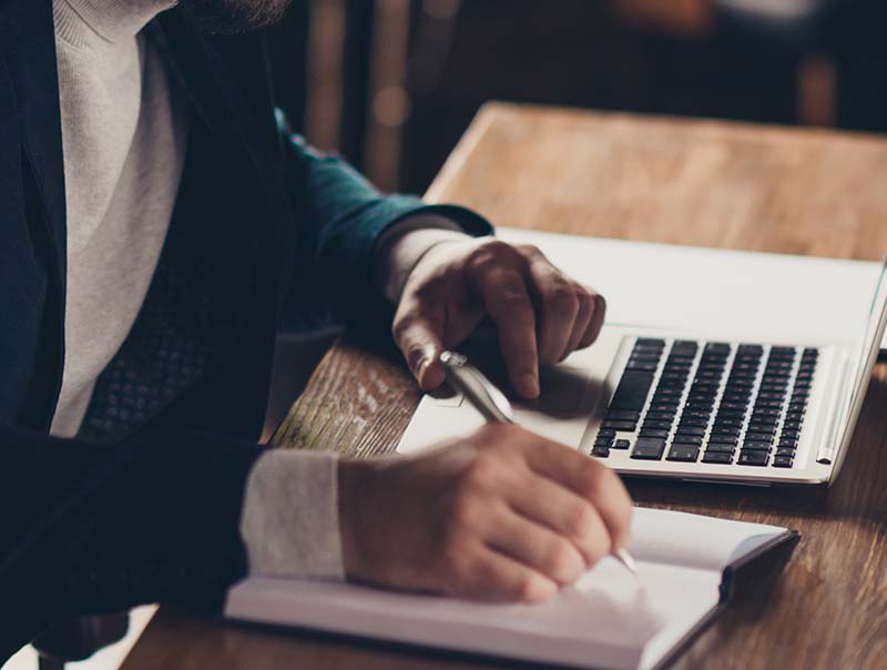 author writing with pen and laptop